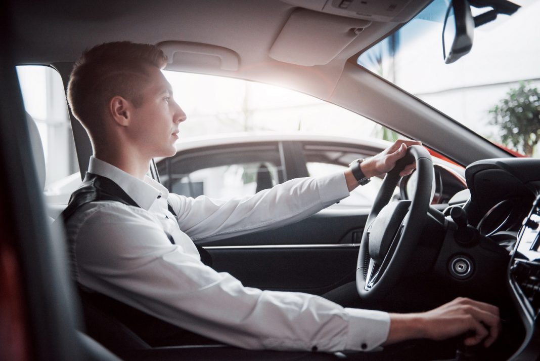 A young man sits in a newly purchased car at the wheel, a successful purchase.