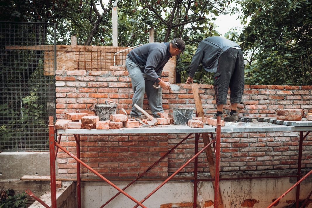 Worker placing and installing bricks on exterior wall on house