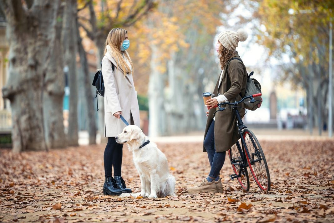 Two friends wearing surgical mask talking and walking with their