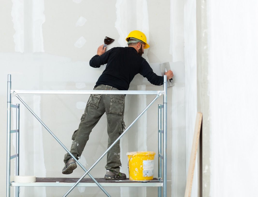 worker plastering gypsum board wall.