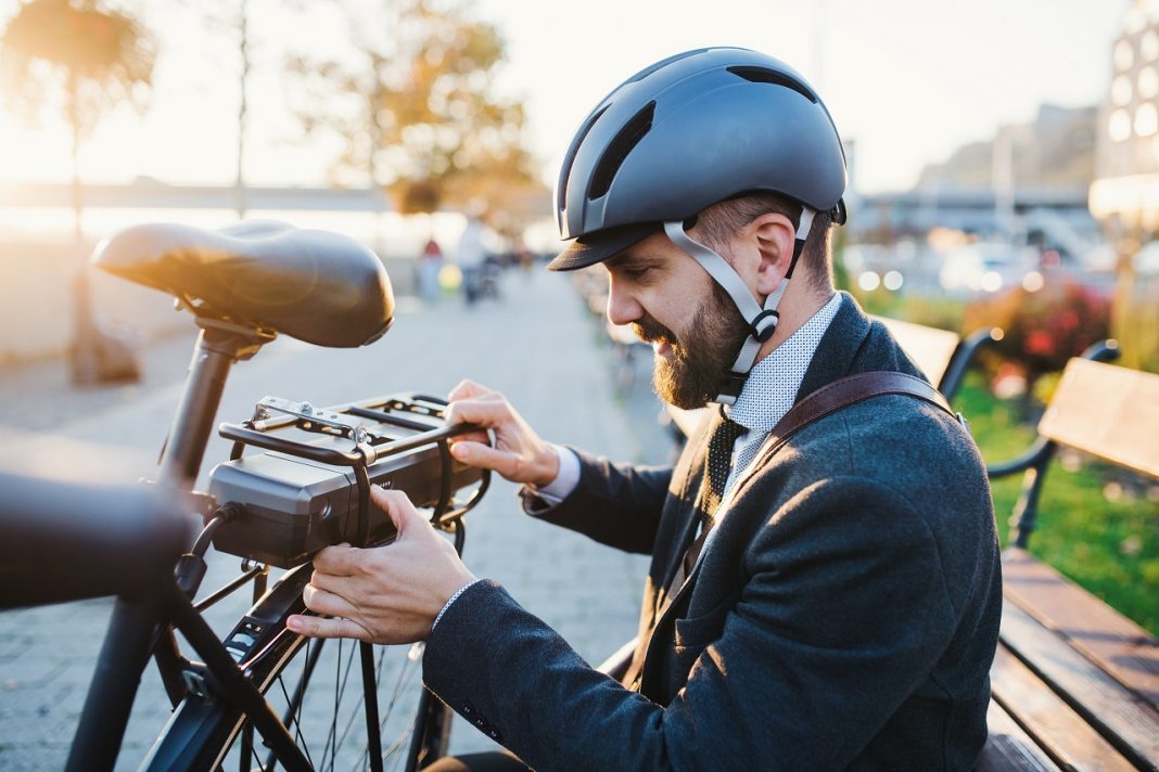 Biciklivel a munkába – mától újra él az elektromos kerékpár pályázat Hipster businessman commuter setting up electric bicycle in city.