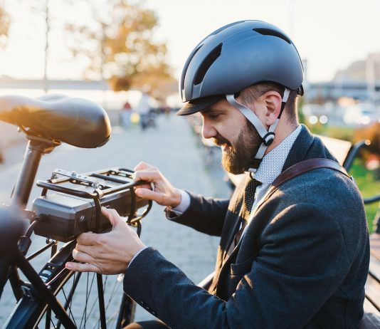 Biciklivel a munkába – mától újra él az elektromos kerékpár pályázat Hipster businessman commuter setting up electric bicycle in city.