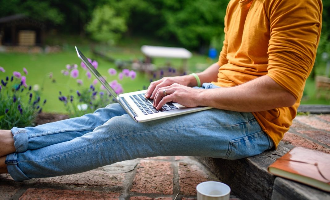 Unrecognizable man with laptop working outdoors in garden, home office concept.
