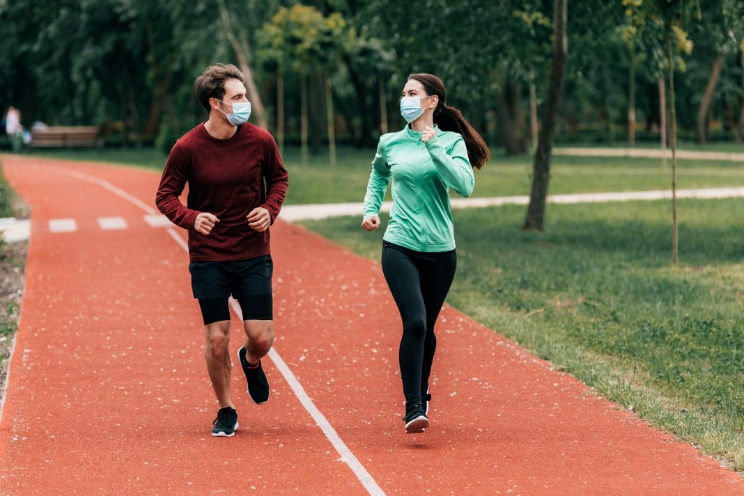 Runners in medical masks looking at each other while training on running track in park