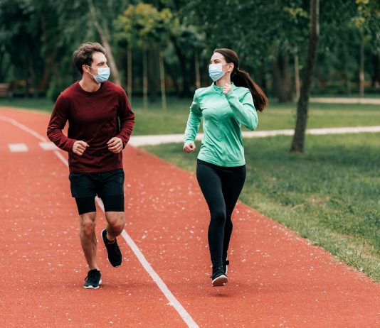 Angliában feloldották a kijárási korlátozásokat Runners in medical masks looking at each other while training on running track in park