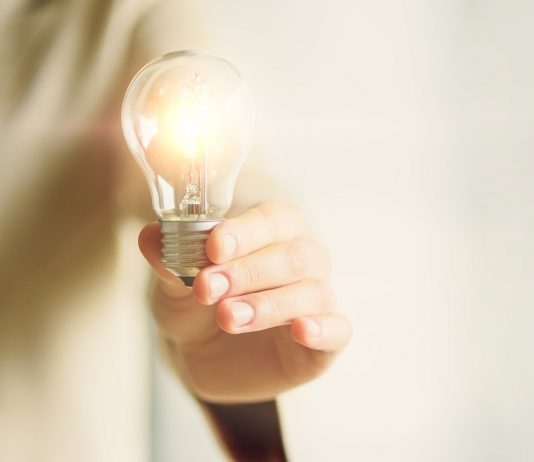 A kisvállalkozók igazi hősök Woman hand holding light bulb on cream background with copy space. Creative idea, new business plan, motivation, innovation, inspiration concept.