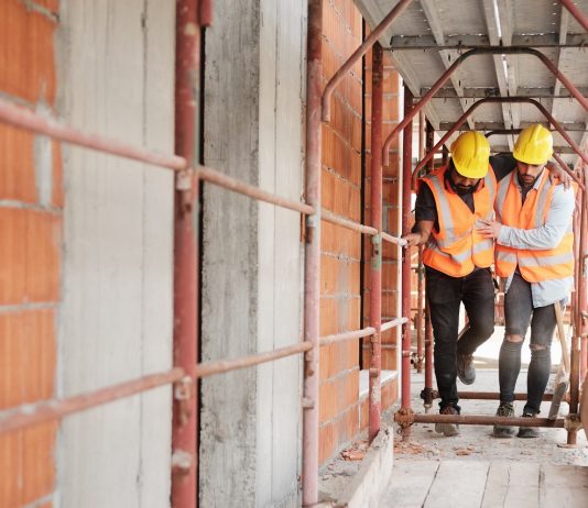 A munkavégzés mint lehetséges veszélyes üzem Manual Worker Helping Injured Colleague In Construction Site