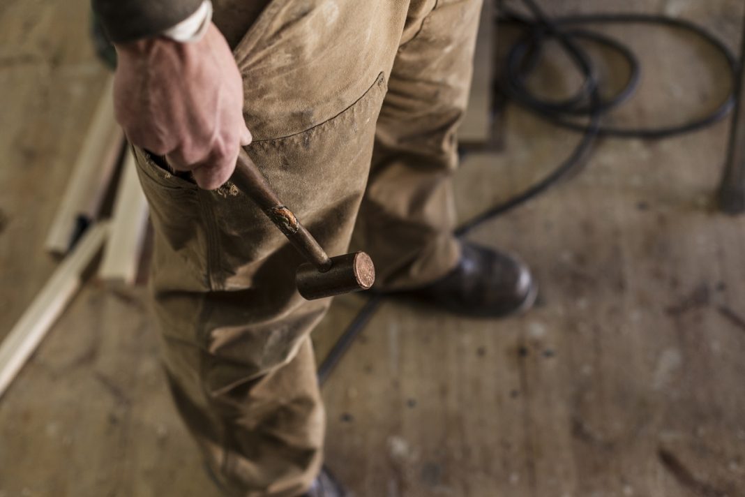 Munka? Na, az nincs kilátásban. Low section of carpenter holding hammer in workshop