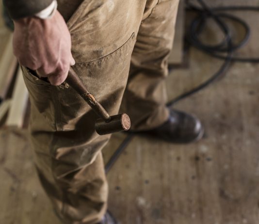 Munka? Na, az nincs kilátásban. Low section of carpenter holding hammer in workshop