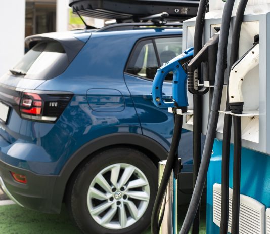 Komoly gazdasági lehetőség rejlik az okos és fenntartható közlekedésben Electric car on gas station. Blue car and electric plug for char