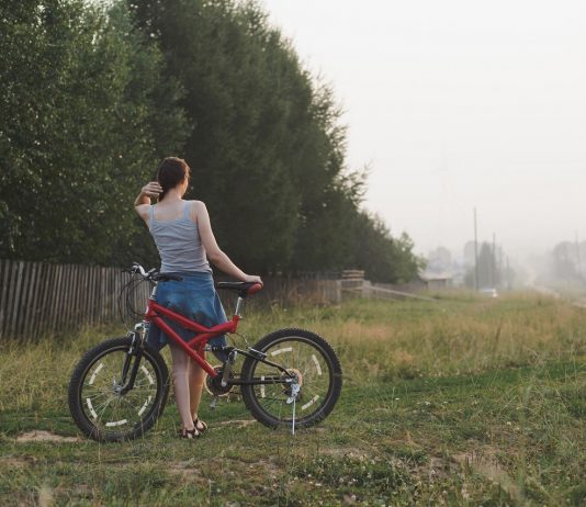 Életmódváltás a láthatáron? Vissza vidékre! young woman standing with bicycle countryside near garden in village