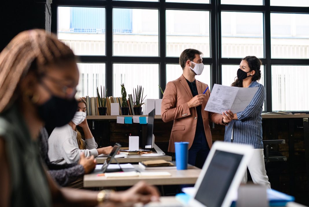 Portrait of young businesspeople with face masks working indoors in office.