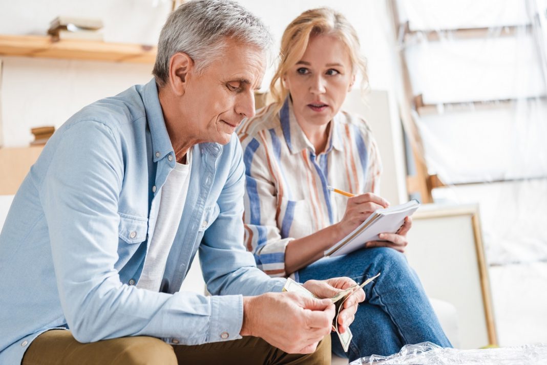serious elderly couple counting money and taking notes during relocation