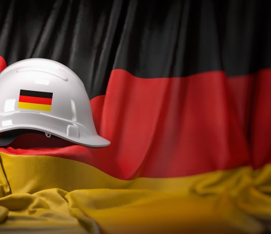 Német munkaerőpiac: tavaszi megújulás a növekvő fertőzésszámok ellenére White hard hat laying over Germany flag. Construction and employ