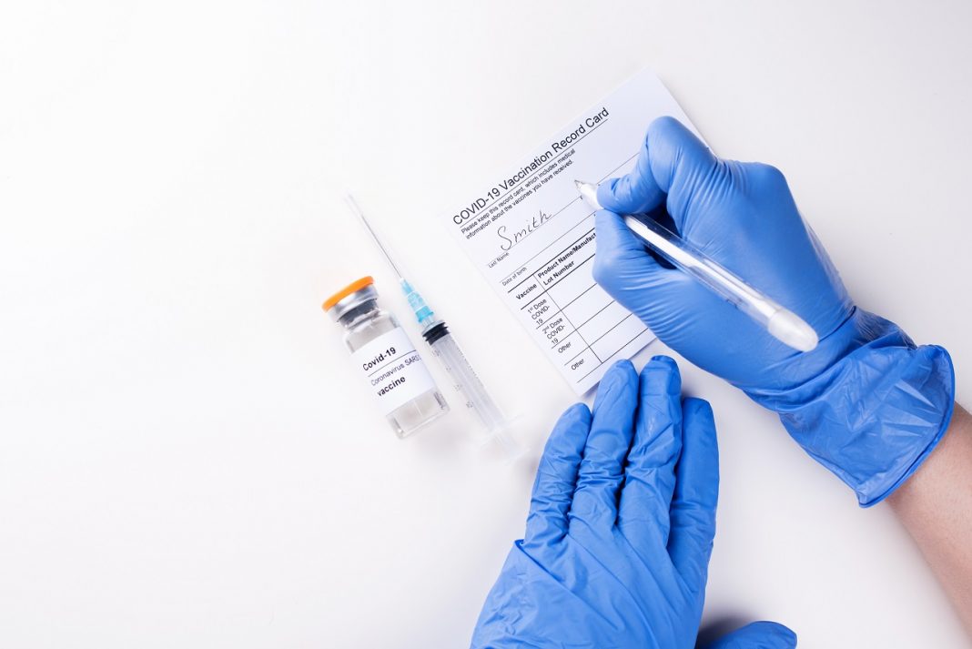 Doctor's hands in medical gloves filling out the vaccination record card.