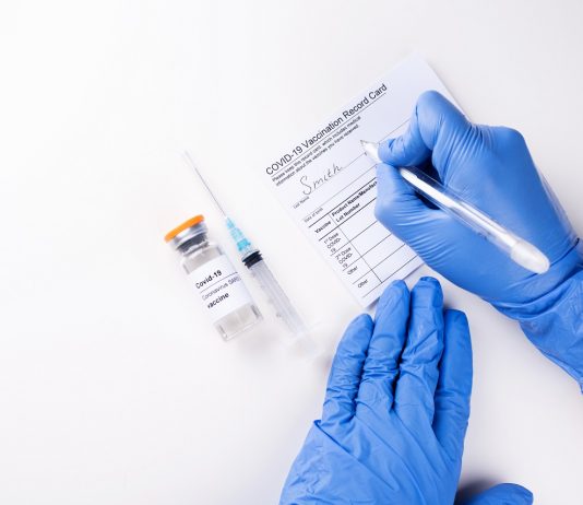 Tudhatja-e a munkáltató, hogy be vagyunk oltva? Doctor's hands in medical gloves filling out the vaccination record card.