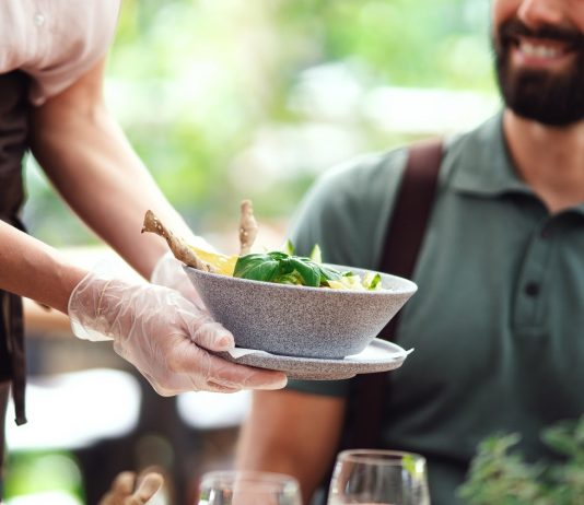 Egy forintért adhatnak fel álláshirdetést a Profession.hu-n a vendéglátás és idegenforgalom szektorban munkaerőt keresők Unrecognizable waitres with gloves serving man outdoors on terrace restaurant.