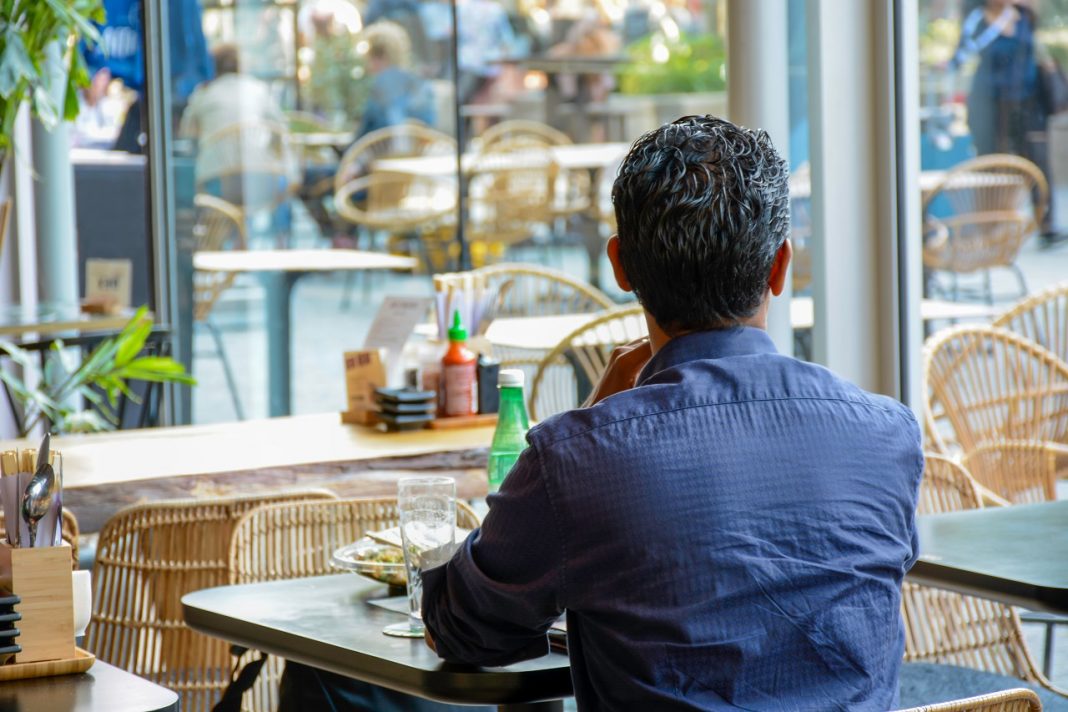 Man from behind sits in a modern restaurant and looks outside. H