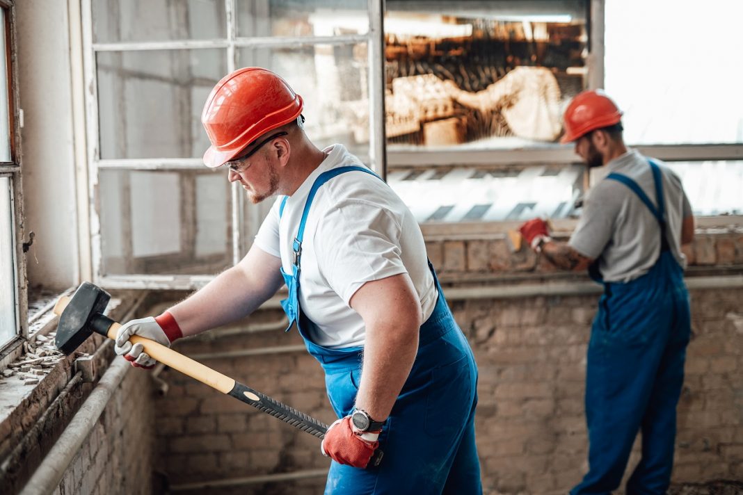 A pair of workers are working to remove plaster from the old walls
