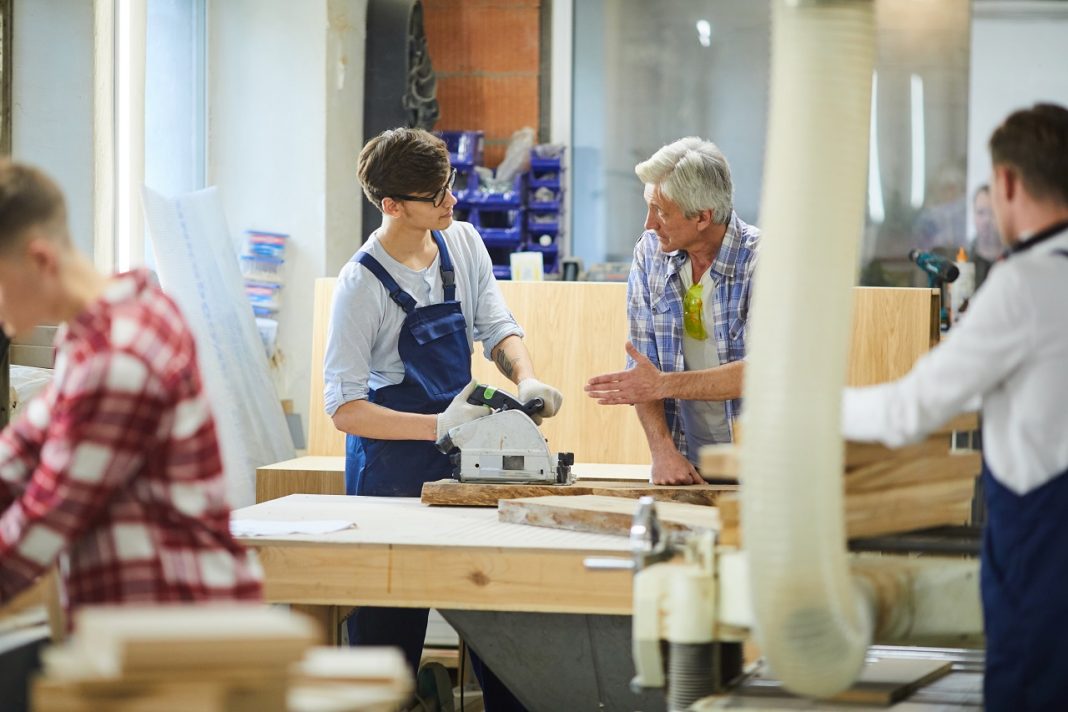 Senior carpenter teaching young worker at factory