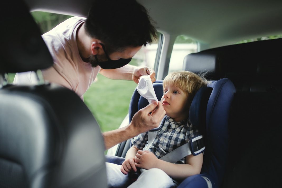 Father with small son going on trip by car, wearing face masks.