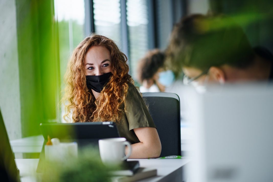 A második első nap Young woman with face mask back at work in office after lockdown.