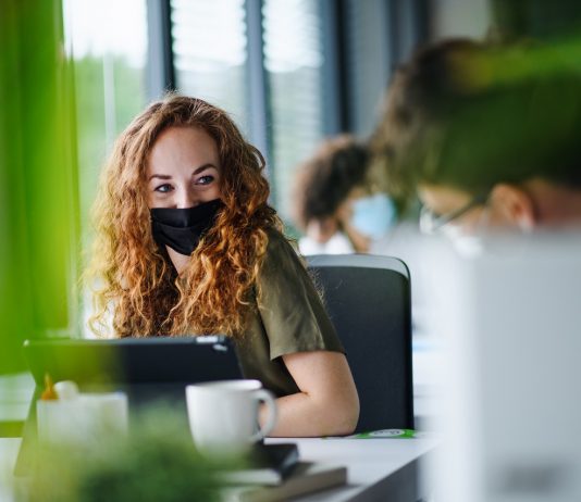 A második első nap Young woman with face mask back at work in office after lockdown.