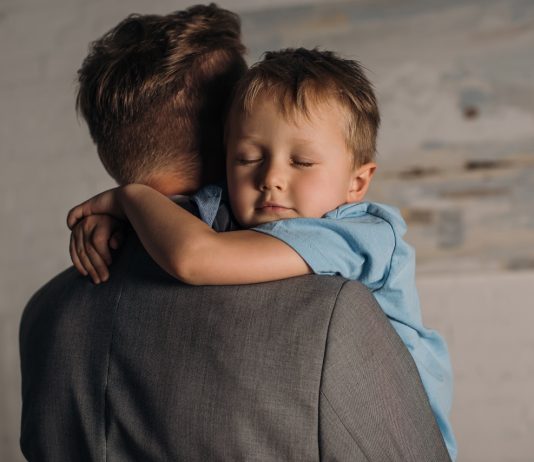 Apák napja: négy extra hét az újdonsült apukáknak little boy with eyes closed hugging father at home