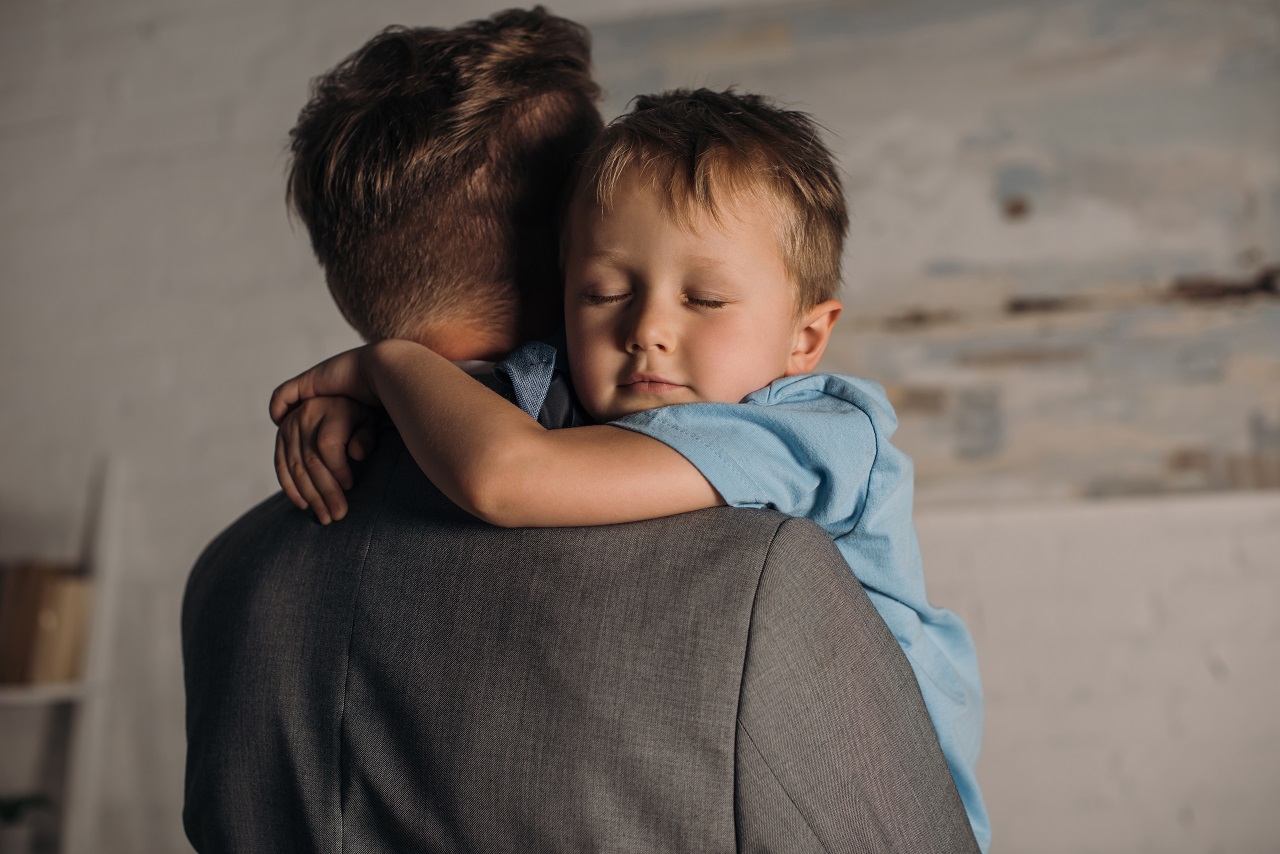 little boy with eyes closed hugging father at home