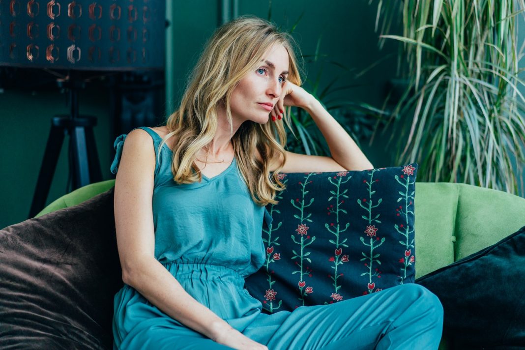 Young attractive Caucasian blonde is sitting bored on the sofa.